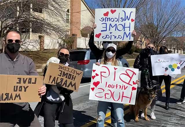 Maria's family and friends holding signs, welcoming her home